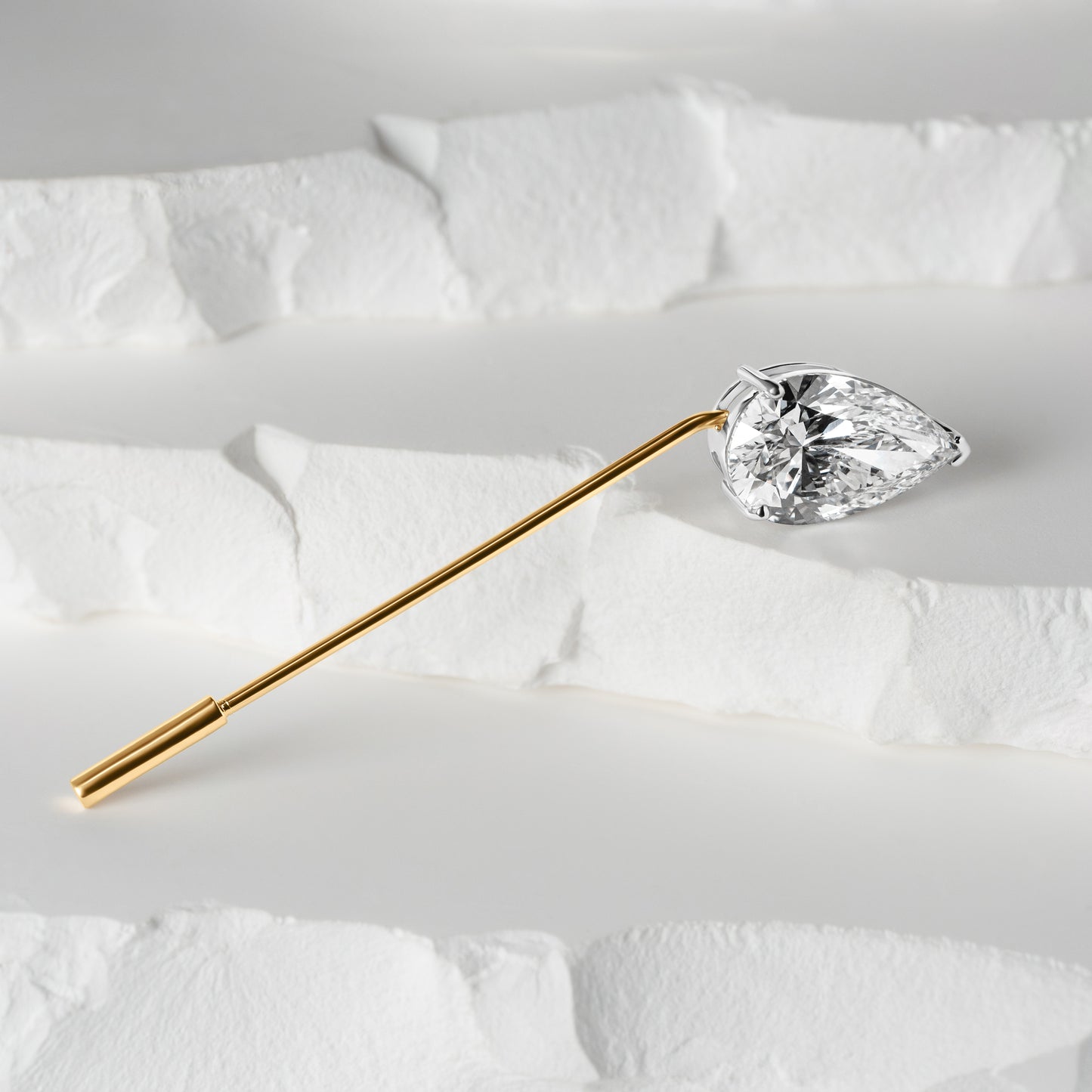 A sleek gold lapel pin featuring a pear-shaped lab-grown diamond, set against a textured white background for an elegant and minimalist display.