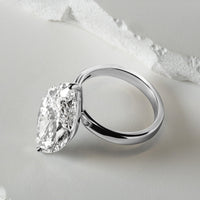 A close-up of a solitaire lab-grown diamond engagement ring with a brilliant oval-cut diamond in a sleek platinum setting, displayed against a textured white background for a refined, modern look.