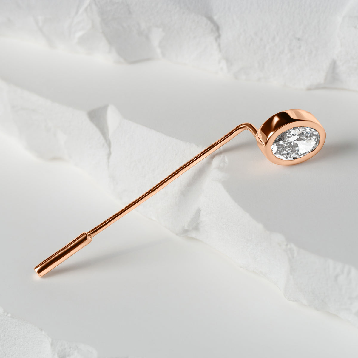 Rose gold lapel pin featuring an oval-cut lab-grown diamond, elegantly displayed on a textured white surface with layered details.